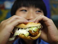 A boy poses with a chicken burger at a fast food outlet in Taipei January 29, 2010. The Taiwan Department of Health proposed a ban on junk food advertisements aired around children's television programmes, to tackle the growing child obesity rate. REUTERS/Nicky Loh.